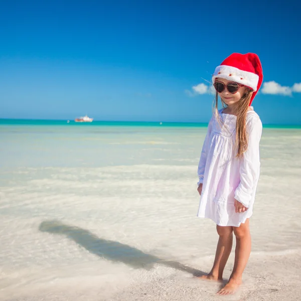 Kleines entzückendes Mädchen mit rotem Weihnachtsmann-Hut am tropischen Strand — Stockfoto