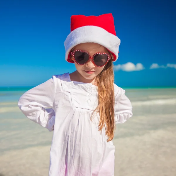 Urocze dziewczynki w czerwonym kapeluszu Santa na tropikalnej plaży — Zdjęcie stockowe