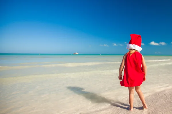 Little adorable girl in red Santa hat at tropical beach — Stock Photo, Image