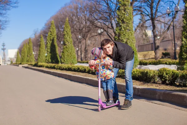 Adorable little girl and happy father ride on scooter outdoors — Stock Photo, Image