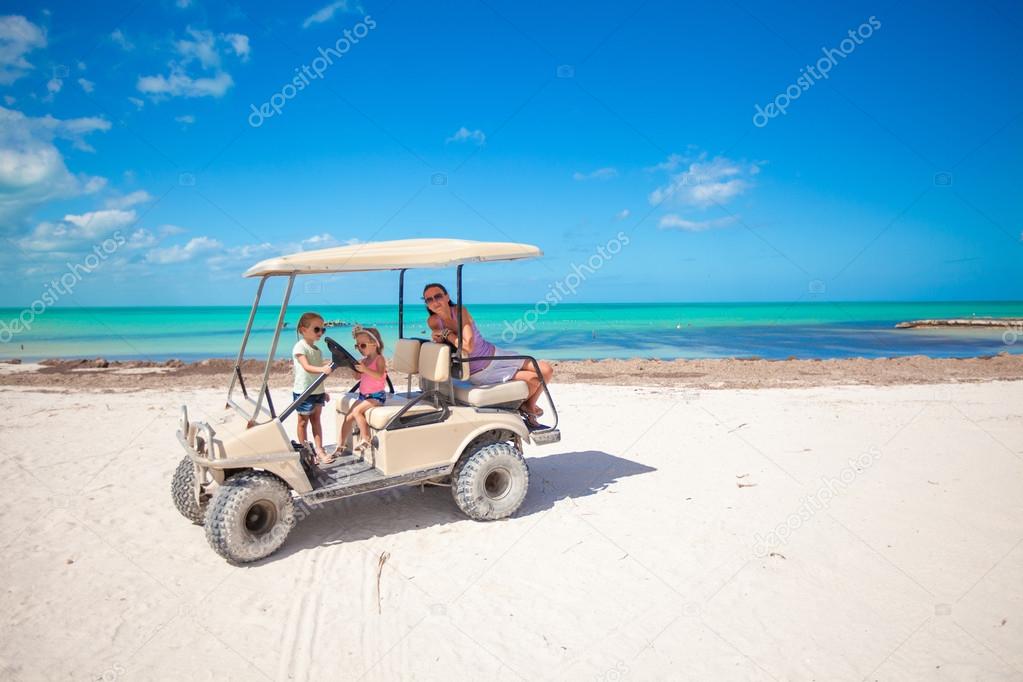 Little girls and their mother driving golf cart at tropical beach