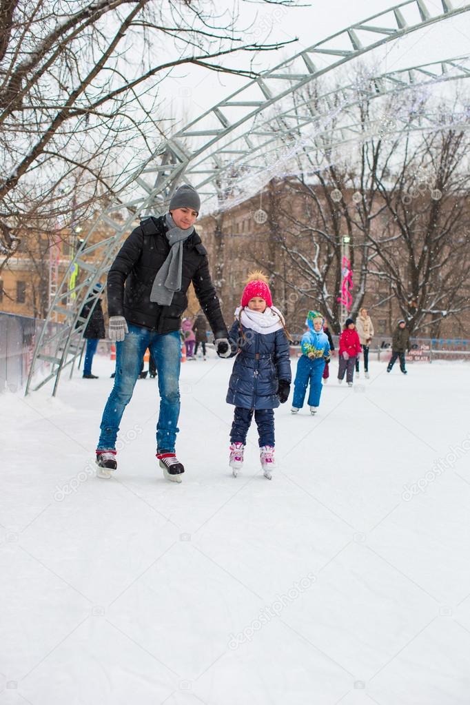 Adorable little girl and happy dad on skating rink outdoor