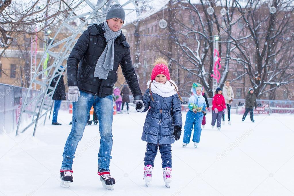 Adorable little girl and happy dad on skating rink outdoor