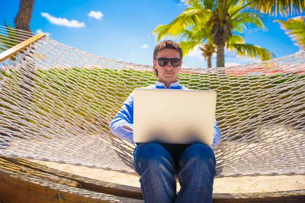 Молодий чоловік працює з ноутбуком в гамаку під час пляжних канікул — стокове фото