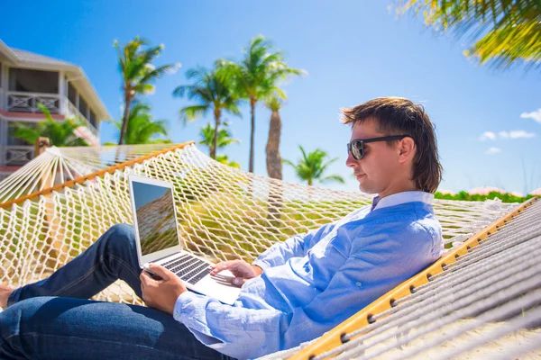 Hombre joven que trabaja con el ordenador portátil en la hamaca durante las vacaciones de playa —  Fotos de Stock