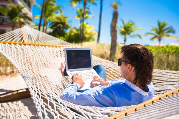 Jovem trabalhando com laptop em rede durante as férias na praia — Fotografia de Stock