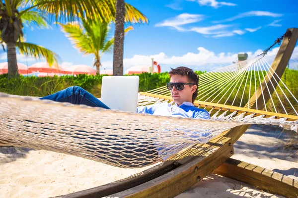 Young man working on laptop in hammock at tropical beach — Stock Photo, Image