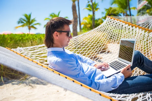 Hombre joven que trabaja con el ordenador portátil en la hamaca durante las vacaciones de playa —  Fotos de Stock