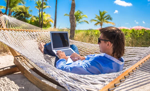 Giovane che lavora con il computer portatile in amaca durante le vacanze al mare — Foto Stock