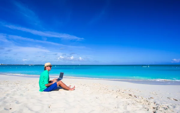 Ung man arbetar på bärbar dator på tropical beach — Stockfoto