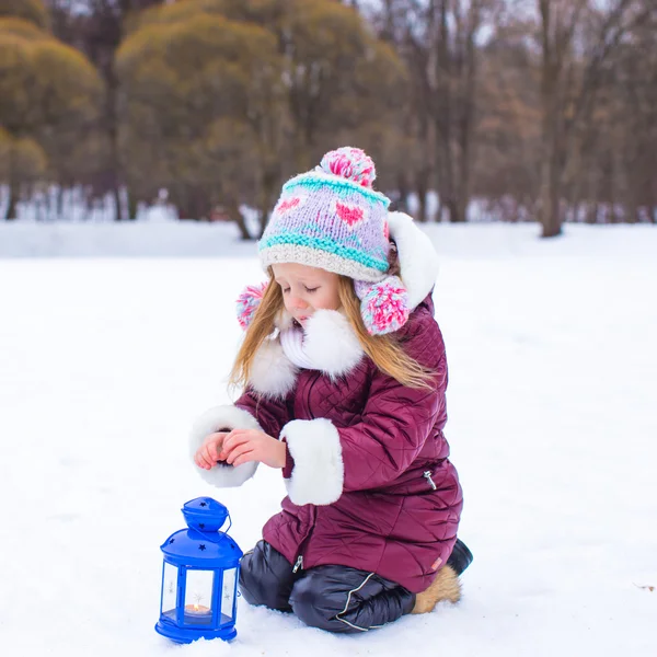Little girl warms hands on candle in lantern outdoors — Stock Photo, Image