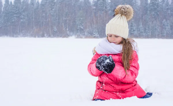 Happy adorable little girl playing snowballs in snowy winter day Stock Photo