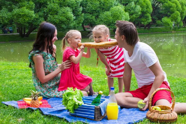 Happy young family picnicking outdoors near the lake — Stock Photo, Image