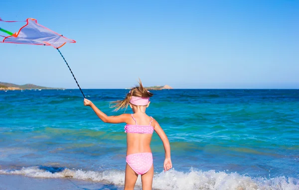 Kleines glückliches Mädchen spielt mit fliegendem Drachen während eines tropischen Strandurlaubs — Stockfoto