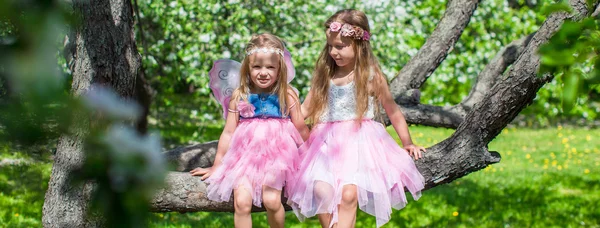 Niñas adorables sentadas en el árbol en flor en el jardín de manzanas —  Fotos de Stock