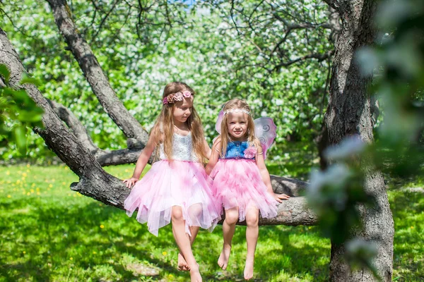 Kleine entzückende Mädchen sitzen auf blühendem Baum im Apfelgarten — Stockfoto