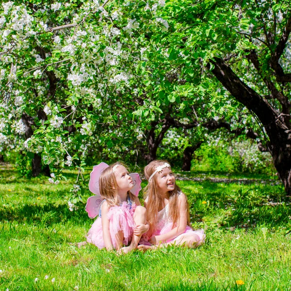 Adorables niñas se divierten en el jardín de manzanos en flor a mayo —  Fotos de Stock