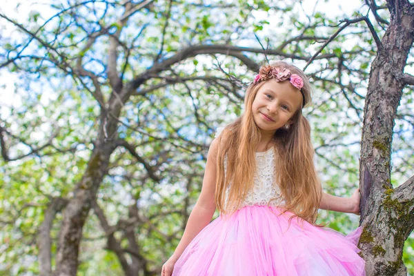 Küçük sevimli kız elma bahçesindeki çiçek açan ağaçta oturuyor. — Stok fotoğraf