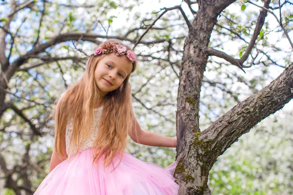 Malá rozkošná dívka sedí na kvetoucím stromě v jablečné zahradě — Stock fotografie