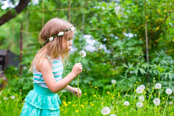 Schattig meisje een paardebloem waait in de tuin — Stockfoto