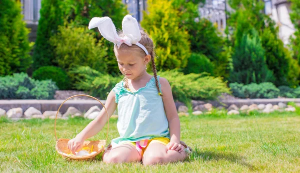 Adorable little girl wearing bunny ears holding basket with Easter eggs — Stock Photo, Image