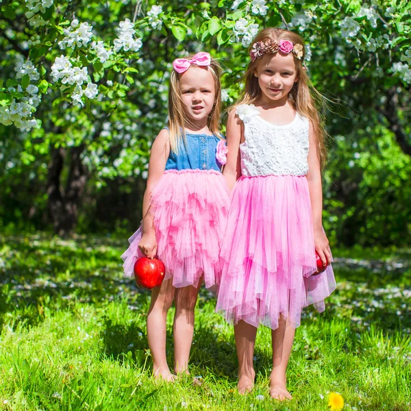 Adorables niñas se divierten en el jardín de manzanos en flor a mayo —  Fotos de Stock