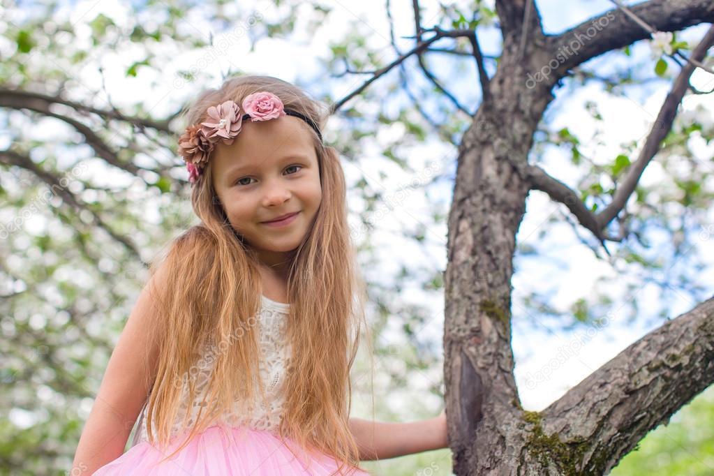 Happy little adorable girl in blossoming apple tree garden
