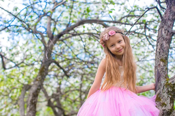 Liten bedårande flicka sitter på blommande träd i äppelträdgård — Stockfoto