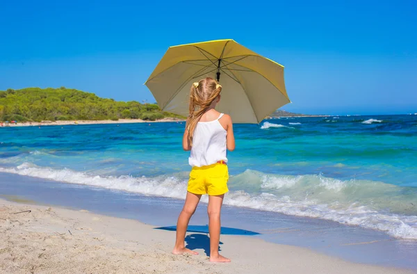 Tropik sahilde büyük sarı şemsiye ile küçük sevimli kız — Stok fotoğraf