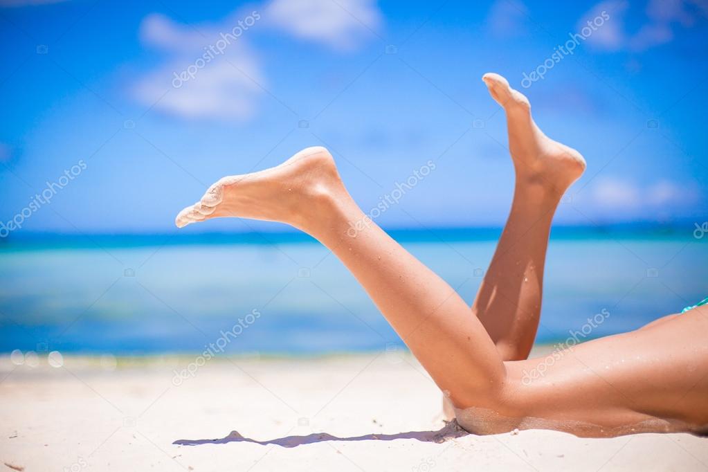 Female tanned slim legs on the white sandy tropical beach