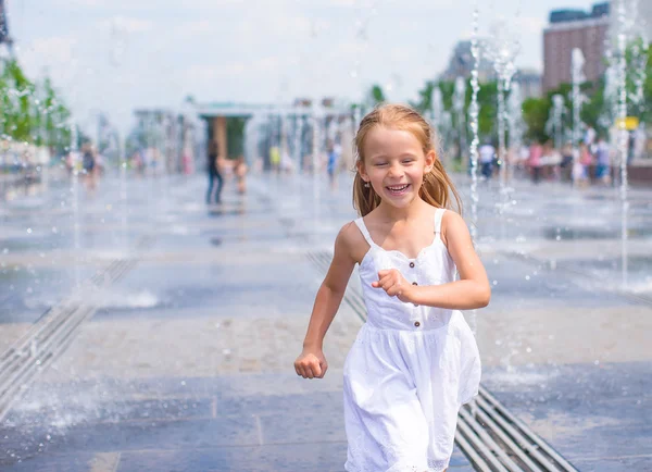 Liten, lykkelig jente morer seg ute i fontenen på varm dag – stockfoto