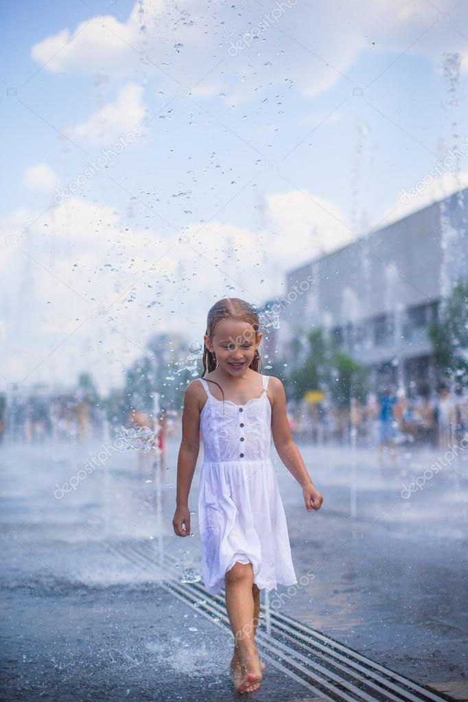 Cute girl having fun in outdoor fountain at hot day