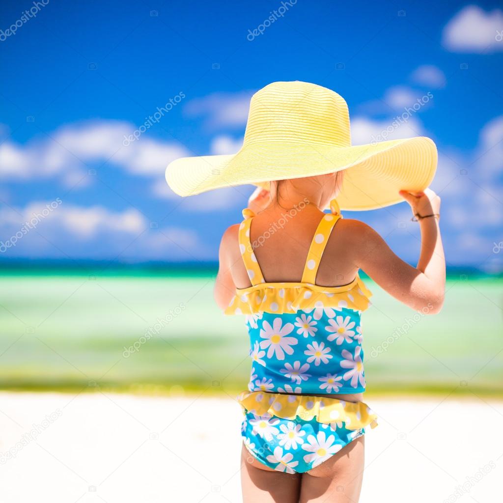 Little girl in big yellow hat on white sandy beach