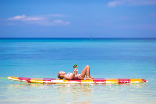 Lille pige med slikkepind har det sjovt på surfbræt i havet - Stock-foto