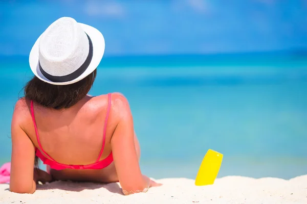 Piękna młoda kobieta trzyma krem do opalania leżący na tropikalnej plaży — Zdjęcie stockowe