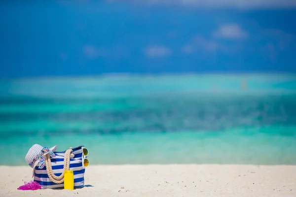 Μπλε τσάντα, λευκό άχυρο καπέλο, flip flop και μπουκάλι αντηλιακό σε τροπική παραλία — Φωτογραφία Αρχείου