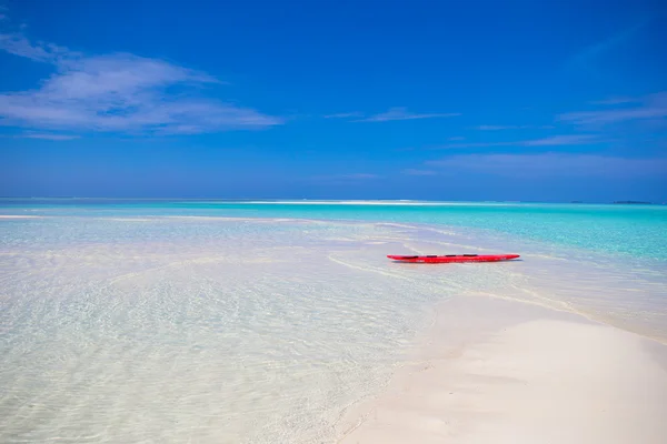 Red surfboard on white sandy beach with turquoise water — Stock Photo, Image