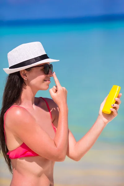 Giovane donna felice che applica lozione abbronzatura sul naso sulla spiaggia bianca — Foto Stock