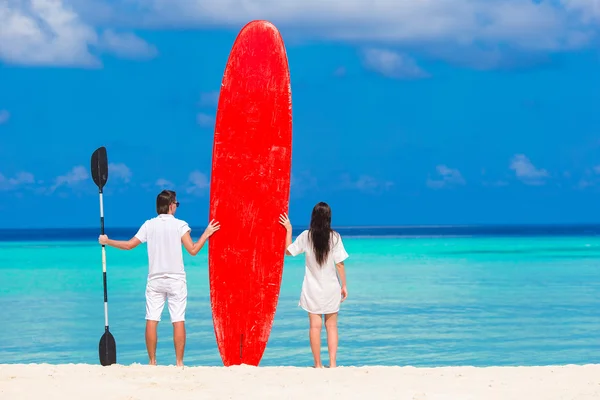 Молодая пара с красной доской для серфинга во время тропических каникул — стоковое фото