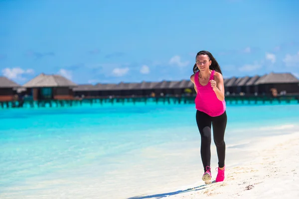 Adatto giovane donna che corre lungo la spiaggia tropicale nel suo abbigliamento sportivo — Foto Stock