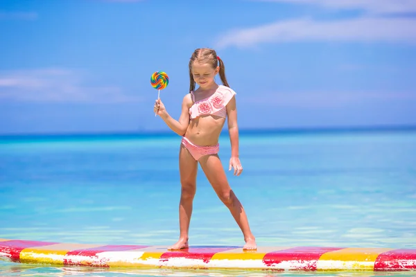 Little girl with lollipop have fun on surfboard in the sea — Stock Photo, Image