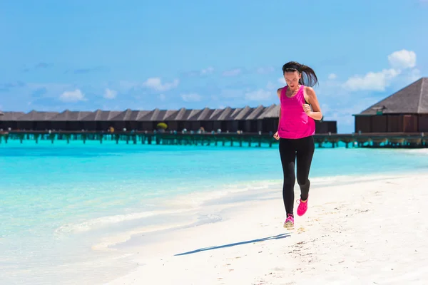 Fit young woman running along the tropical beach in her sportswear — Stock Photo, Image