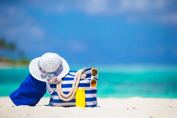 Сумка с голубой полосой и полотенце, соломенная белая шляпа, солнцезащитные очки, бутылка с солнцезащитным кремом на экзотическом пляже — стоковое фото