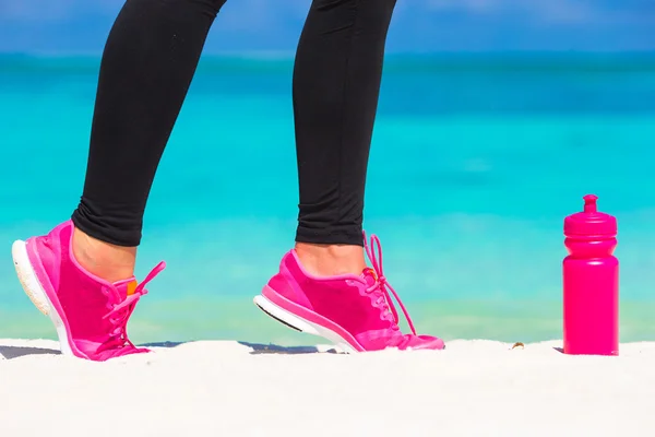 Close-up van vrouwelijke benen in sneakers uitgevoerd op witte zandstrand — Stockfoto