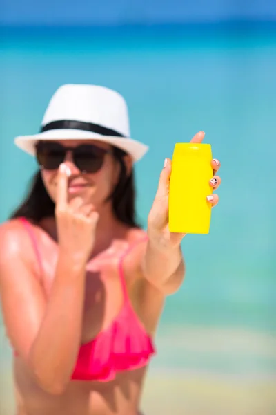 Jovem mulher feliz aplicando loção bronzeado do sol em seu nariz na praia branca — Fotografia de Stock