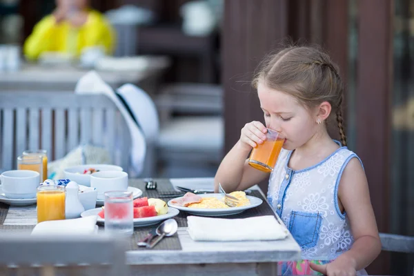Rozkošná holčička pije jablečný džus k snídani v kavárně venkovní — Stock fotografie