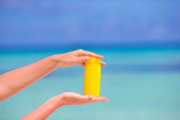 Manos femeninas con crema solar botella fondo azul mar — Foto de Stock