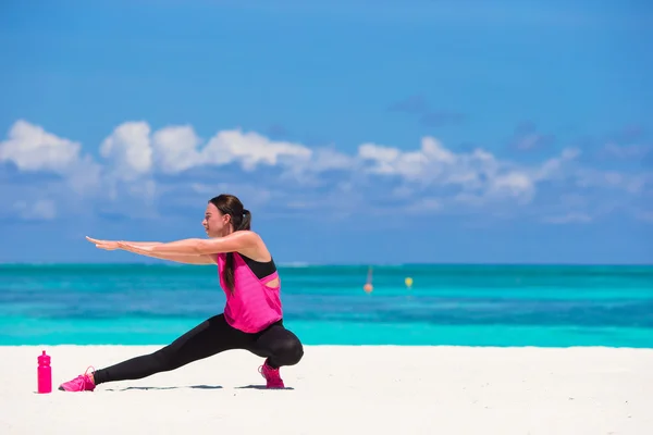 Fit young woman doing exercises on tropical white beach in her sportswear — Stock Photo, Image