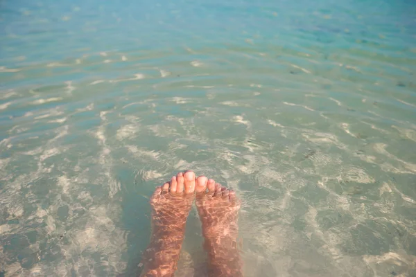 Frauenfüße am weißen Sandstrand und klarem Wasser — Stockfoto