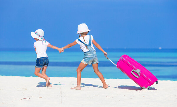 Little adorable girls with big suitcase on tropical white beach during summer vacation